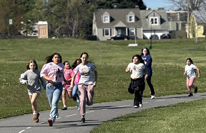 Girls Have Heart Program - A group of children running together on a path in a park on a sunny day.