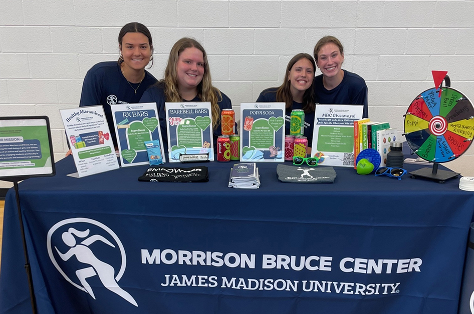 JMU students wearing Morrison Bruce Center shirts and setting at a table full of MBC flyers and merch