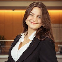 A professional portrait of Eve Elliott in a business suit smiling confidently in an office environment.