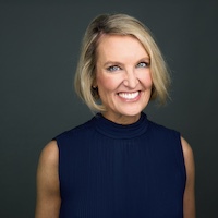 Professional headshot of a smiling woman with short blonde hair, wearing a sleeveless dark blue top.