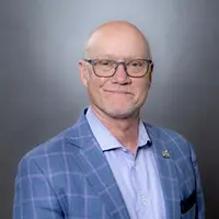 Professional headshot of Charles Potts wearing glasses and a light blue blazer with a checkered pattern.