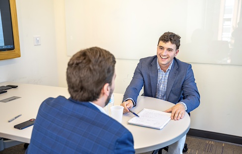 One of the center's corporate partners sits across from a student in an internal sales competition. Both are blue suits.