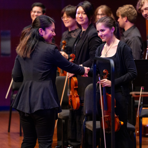 Woman shakes hands with concermaster violinist.