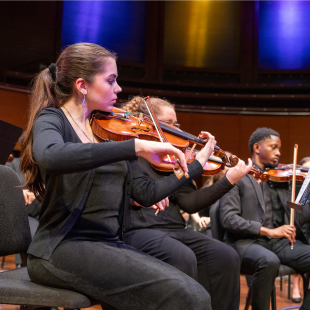 Woman playing violin on stage with orchestra