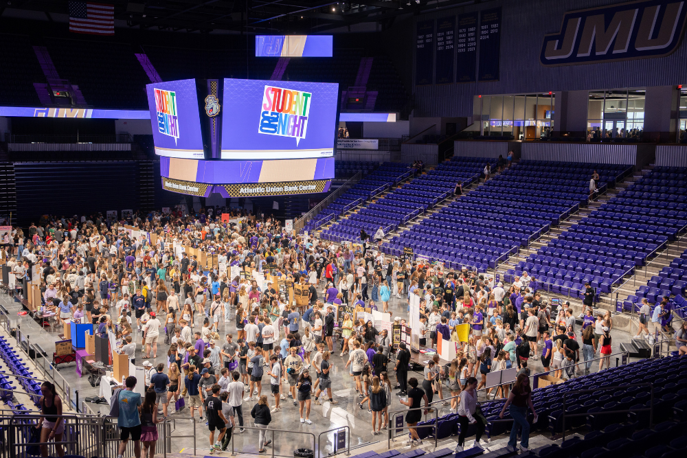 a view of student org night from above inside of JMU's basketball stadium. Students surround tables of various orgs