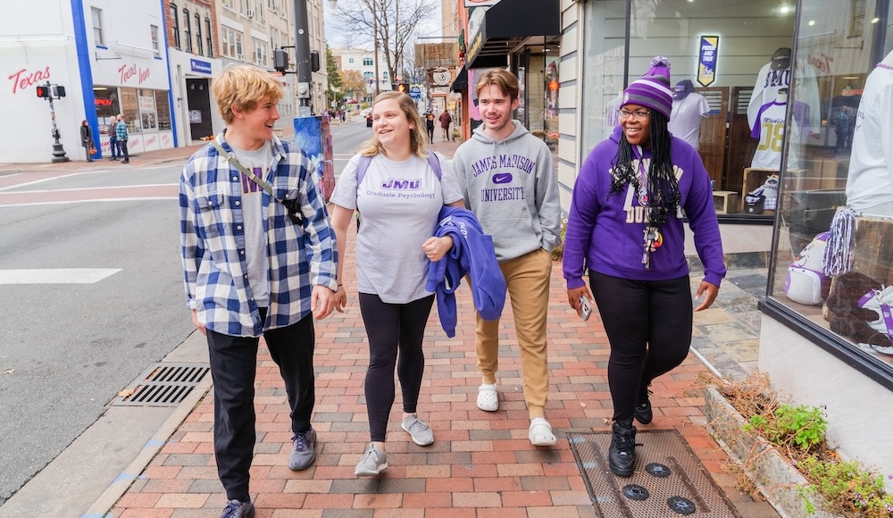 A group of four college students walking together on a city street, dressed in casual attire that reflects their school spirit.