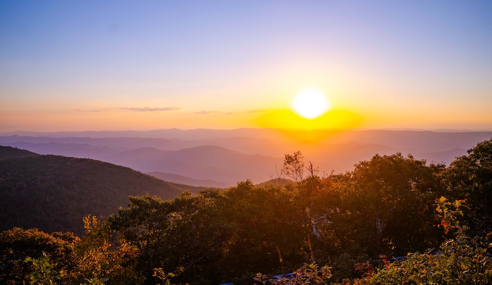 A stunning landscape at sunset, showcasing layered mountains and a vibrant sky filled with warm hues.