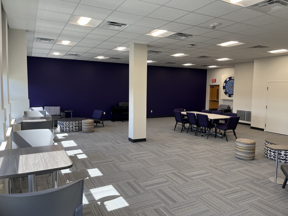 A clean open view of the interfaith space in the Union with a number of various-sized tables with chairs around them, looking toward a purple wall