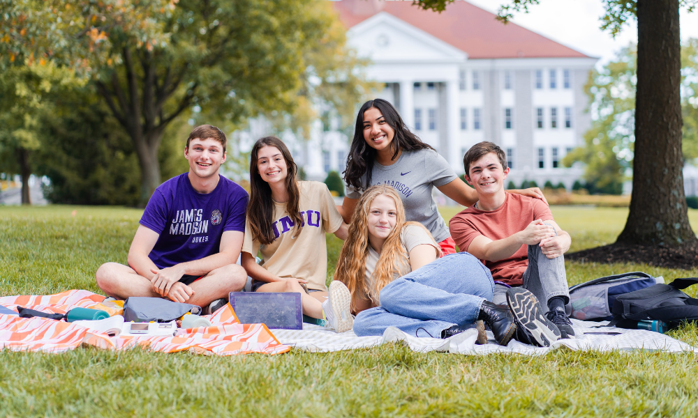 A group of students posing for a picture on the quad. Some are laying on blankets on the grass