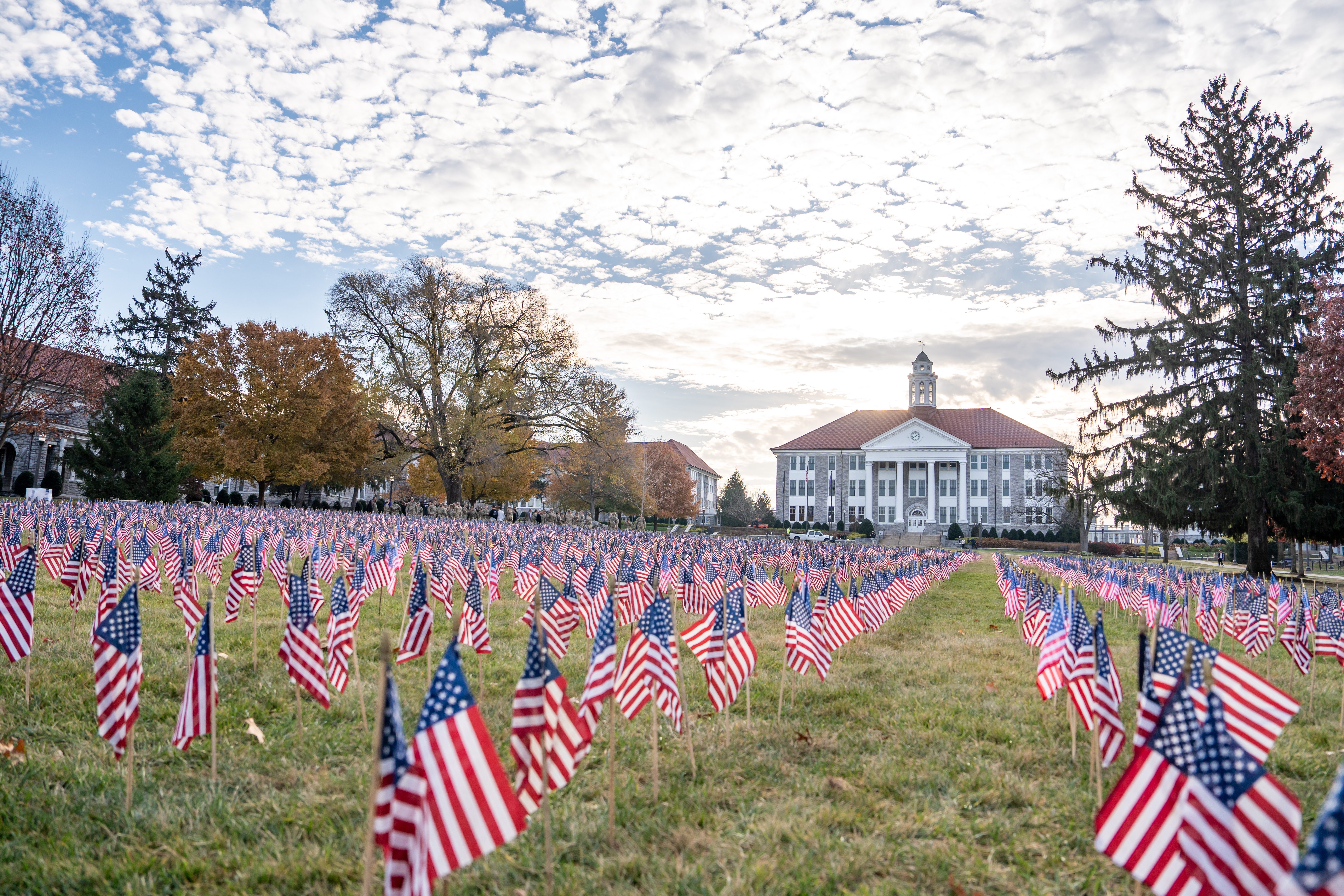 A photo of individuals wearing their military uniforms, holding flags while running onto JMU's football field.