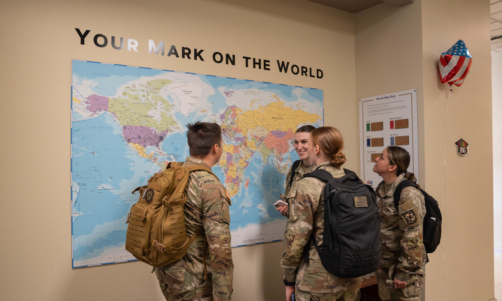 A photo of four individuals wearing their military uniforms, and talking to each other in front of a world map.