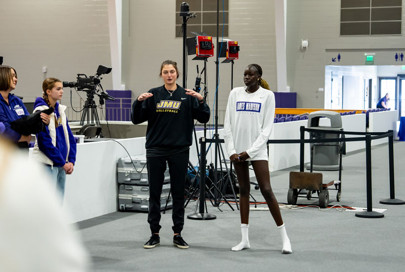 Two volleyball players stand in a gymnasium setting