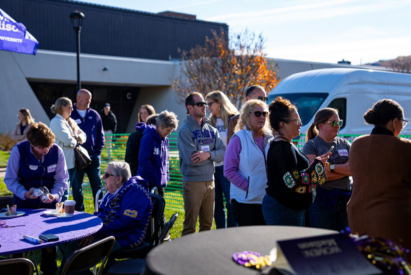 A crowd of people engaged in an outdoor event, with some gathered around tables and others standing in line.